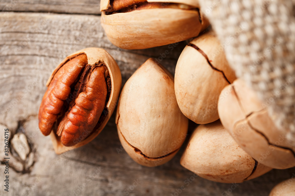 Fototapeta premium Pecans spill out of a bag on a wooden table, close-up. Peeled, in a shell.