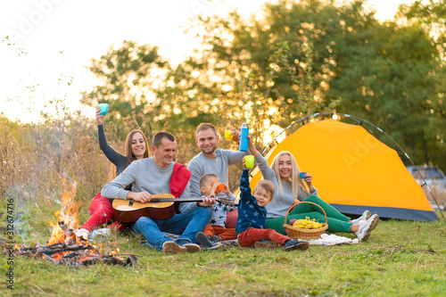 travel, tourism, hike, picnic and people concept - group of happy friends with tent and drinks playing guitar at camping