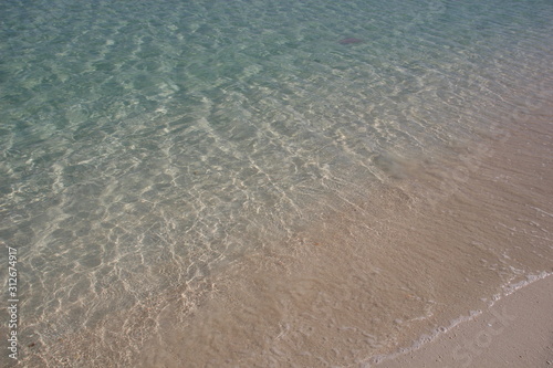 Calm sea water on white sand blinking in day sun
