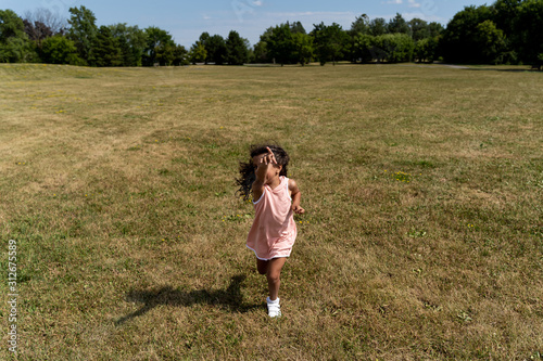 Young girl in pink dress and running in a park seen from behind