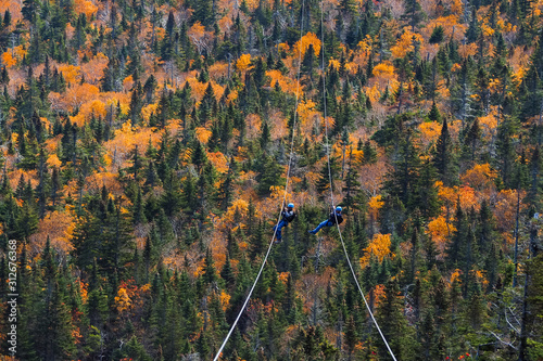 two people sliding down very long and fast zipline during autumn in Stowe, Vermont