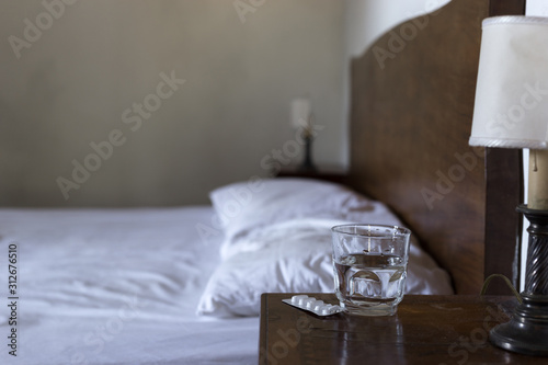 Fotografía Water glass, a pack of tablets / pills and a bed in the blurred background