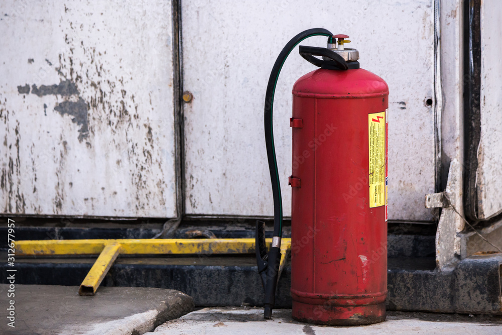 Red Fire extinguisher standing next to a white damaged building Red Fire extinguisher standing next to a white damaged building