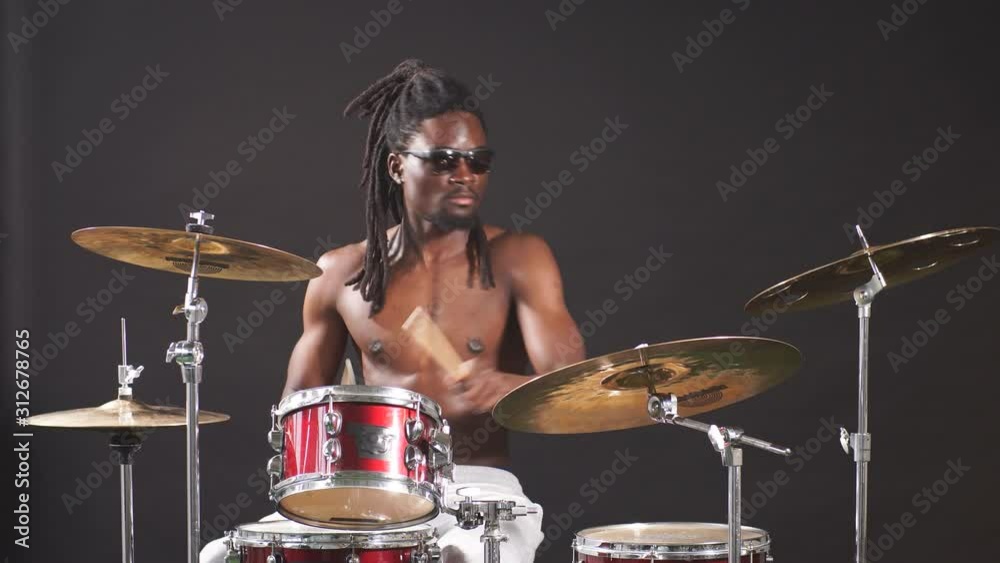 Professional african drummer man playing on drums and cymbals, wearing eyeglasses and holding sticks.