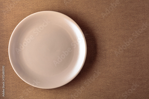 Empty ceramic round beige plate on a beige tablecloth.