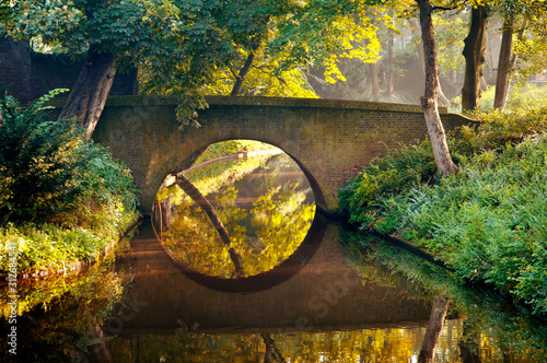 Stone old bridge reflection in the form of a circle in water of a canal in a park, Den Bosch, The Netherlands