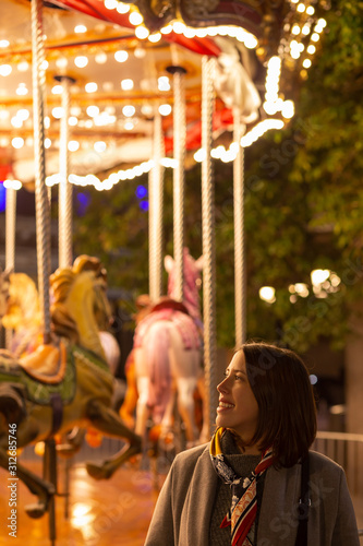 young woman standing next to a vintage carousel at night