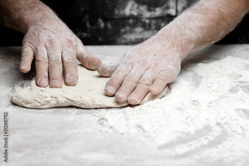Hands of male baker preparing yeast dough with white flour dust on black background, scoop out for pasta and pizza