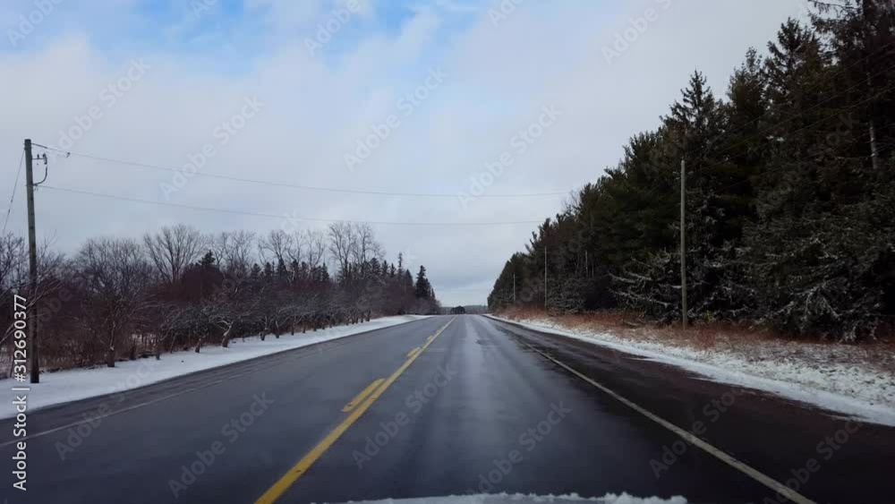 Driving Rural Countryside Road in Winter With Snow on Side of Road in Day. Driver Point of View POV Driving Street With Snow on Trees With Overcast Cloud Sky. Driving Rural Countryside Road in Winter With Snow on Side of Road in Day. Driver Point of View POV Driving Street With Snow on Trees With Overcast Cloud Sky.