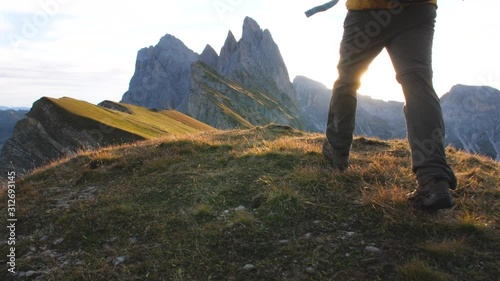 Young man hiking at Seceda mountain arriving to peak at sunrise. Backpack, yellow jacket, boots, beanie. Traveling to puez Odle, Dolomites, Trentino, Italy. photo