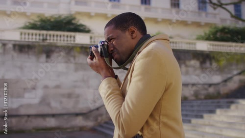 Camera circles a photographer with a retro film camera as he takes pictures, in slow motion