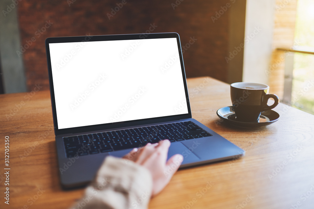 Mockup image of a woman using and touching on laptop touchpad with blank white desktop screen with coffee cup on wooden table Mockup image of a woman using and touching on laptop touchpad with blank white desktop screen with coffee cup on wooden table