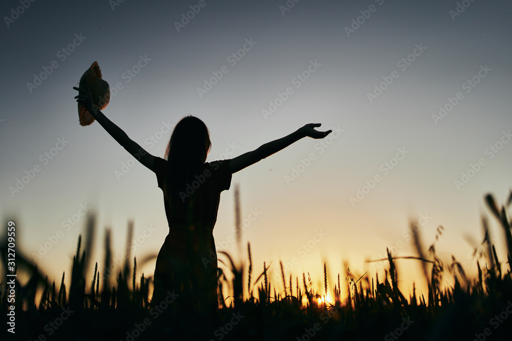 silhouette of young woman with arms raised at sunset