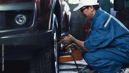 car mechanic in uniform at garage and service station checking and having wheels and tires maintenance service