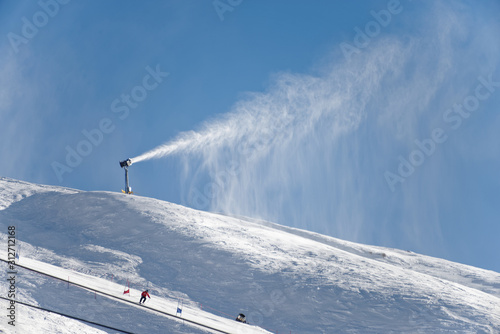 A snow canon shoots out fresh snow on a mountain ski field