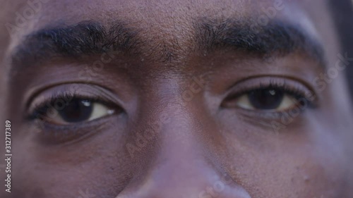 Close up portrait of black male's eyes opening before smiling to camera, in slow motion photo