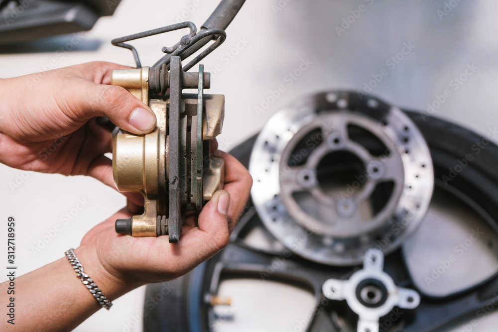 Motorcycle mechanic check brake discs, Brake pads front Brake system at garage ,motorcycle maintenance and repair concept.selective focus Motorcycle mechanic check brake discs, Brake pads front Brake system at garage ,motorcycle maintenance and repair concept.selective focus
