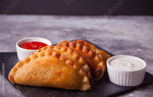 Fied meat pies empanadas cheburek with dips on the black plate.