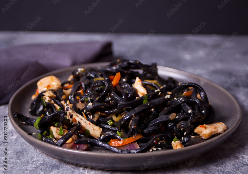 Black squid ink udon noodles with chicken meat on the black plate on dark stone background. Black squid ink udon noodles with chicken meat on the black plate on dark stone background.
