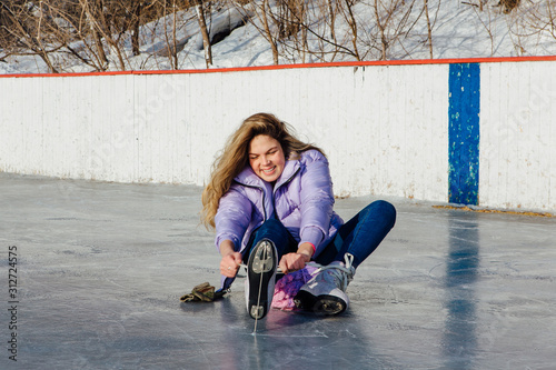 Lovely young woman sitting on ice ring and tieing shoelaces