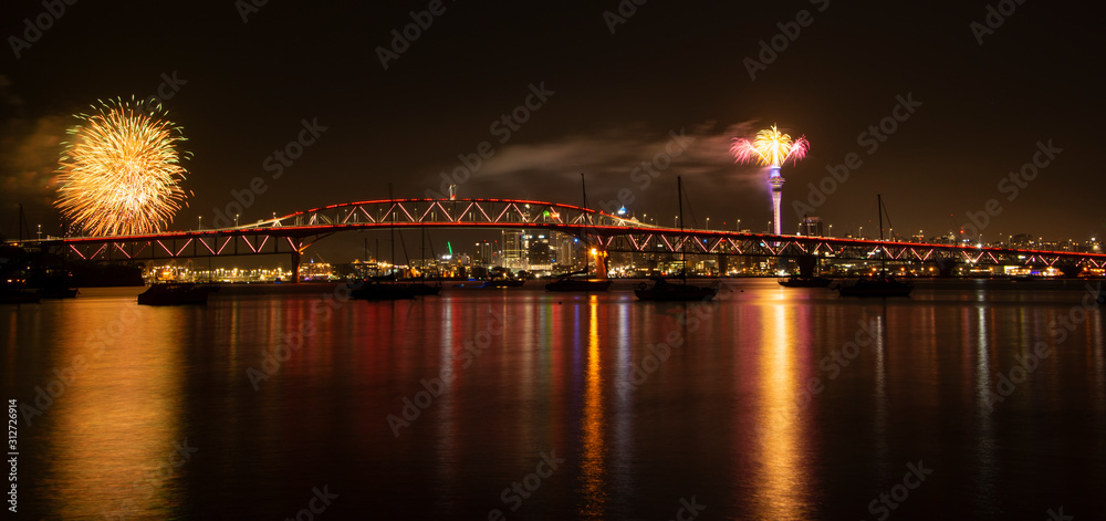Auckland Sky Tower fireworks for New Year celebration with Harbor bridge illuminated in red