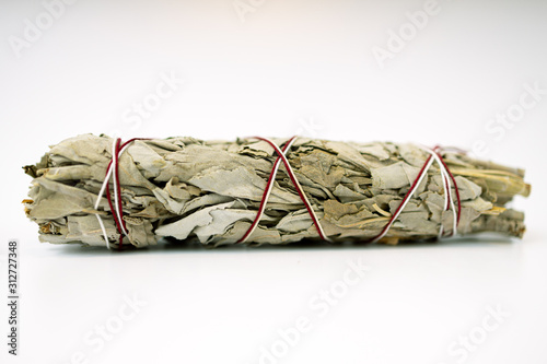 Unburned white sage smudge stick tied with white and red string isolated on white background horizontal in middle of frame. 