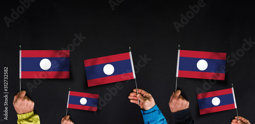 Fototapeta Naklejka Na Ścianę i Meble -  Hands holds flags of Laos on dark background