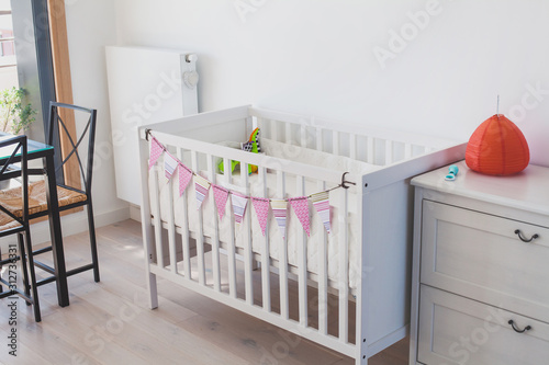 white baby bed crib in child room interior, decorated with paper handmade garland, scandinavian style design