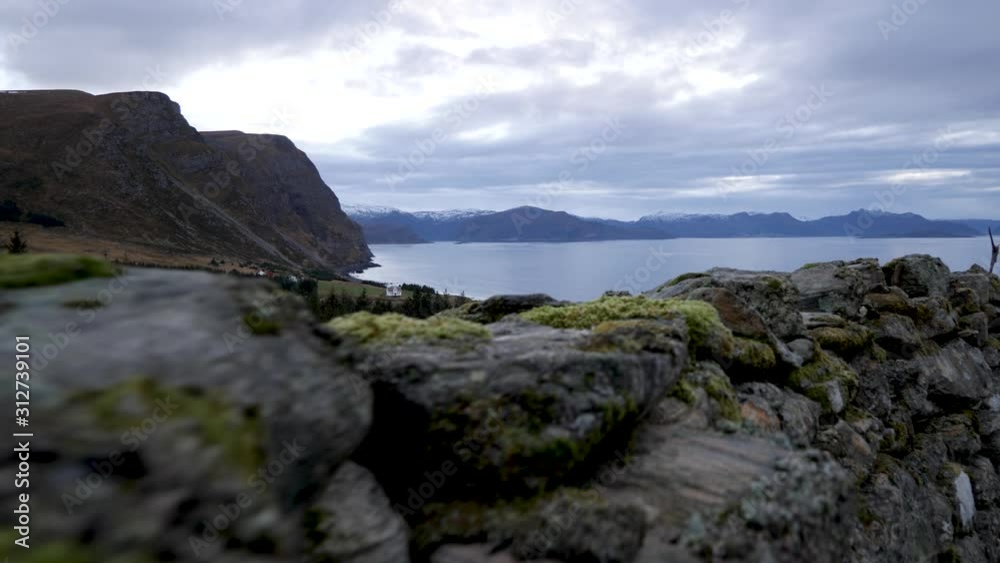 Moving along an ancient stone fence with moss growing on it and overlooking the bay with shepherd fields and mountains in the distance Moving along an ancient stone fence with moss growing on it and overlooking the bay with shepherd fields and mountains in the distance