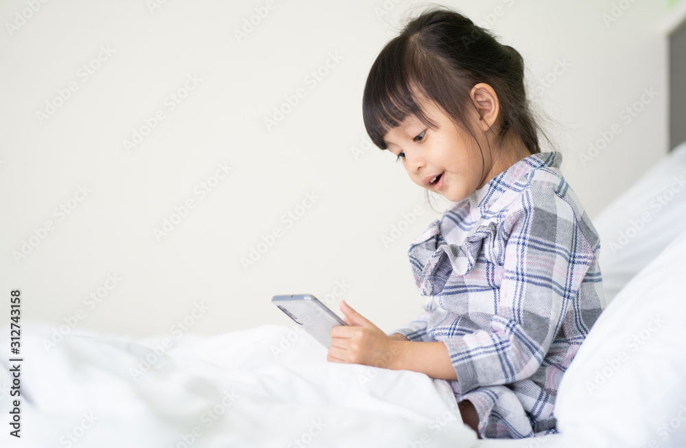Adorable 4 years old asian little girl is sitting on the bed and watching cartoon in the smartphone with happy moment, concept of self control ability for kid to use techonology for trendy lifestyle. Adorable 4 years old asian little girl is sitting on the bed and watching cartoon in the smartphone with happy moment, concept of self control ability for kid to use techonology for trendy lifestyle.