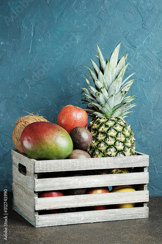 Fresh summer fruits in wooden box on blue background photo