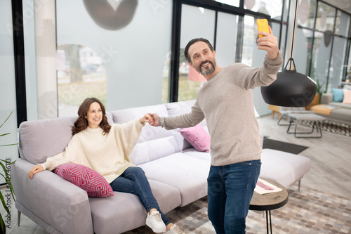 Couple having good time in the furniture salon making selfie