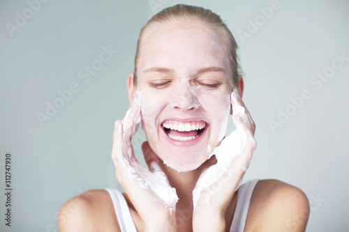 Woman cleaning her skin and washing her face whilst laughing. Foaming facial.