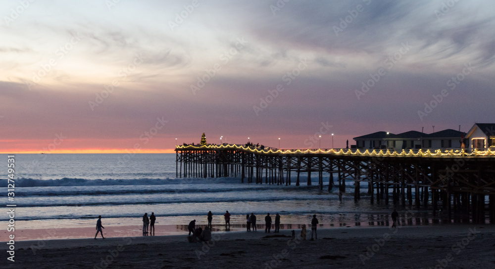 Beachgoers watch sunset  near Crystal Pier in San Diego