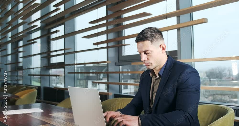 Concerned man working on laptop computer and looking away thinking solving problem at office. Serious athletic male working with notebook