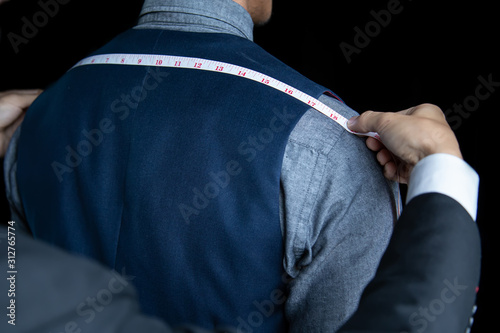 The dressmaker was measuring the width of the back of the man wearing a blue suit on black background. photo