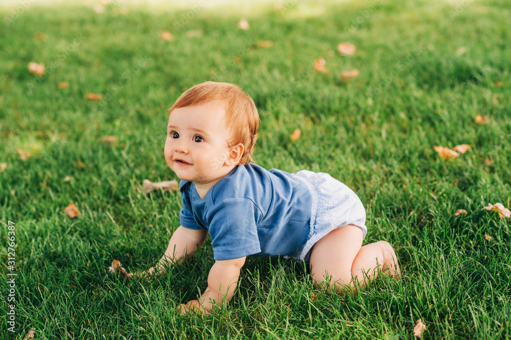 Adorable red haired baby boy crawling on fresh green grass in summer park Adorable red haired baby boy crawling on fresh green grass in summer park