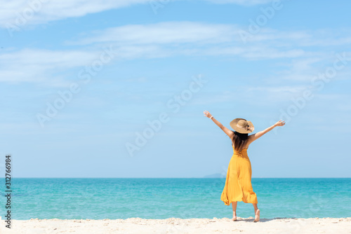 Summer Holiday. Lifestyle woman chill holding big white hat and wearing yellow dress fashion summer trips standing chill on the sandy ocean beach. Happy people enjoy and relax vacation.   copy space