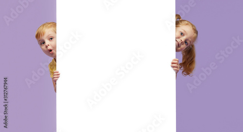 Two little children holding a white banner on purple background. Funny Faces photo