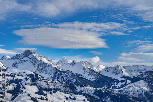 snowy swiss alps mountains in the sun in a blue sky with ufo shaped clouds © youpi4.fc