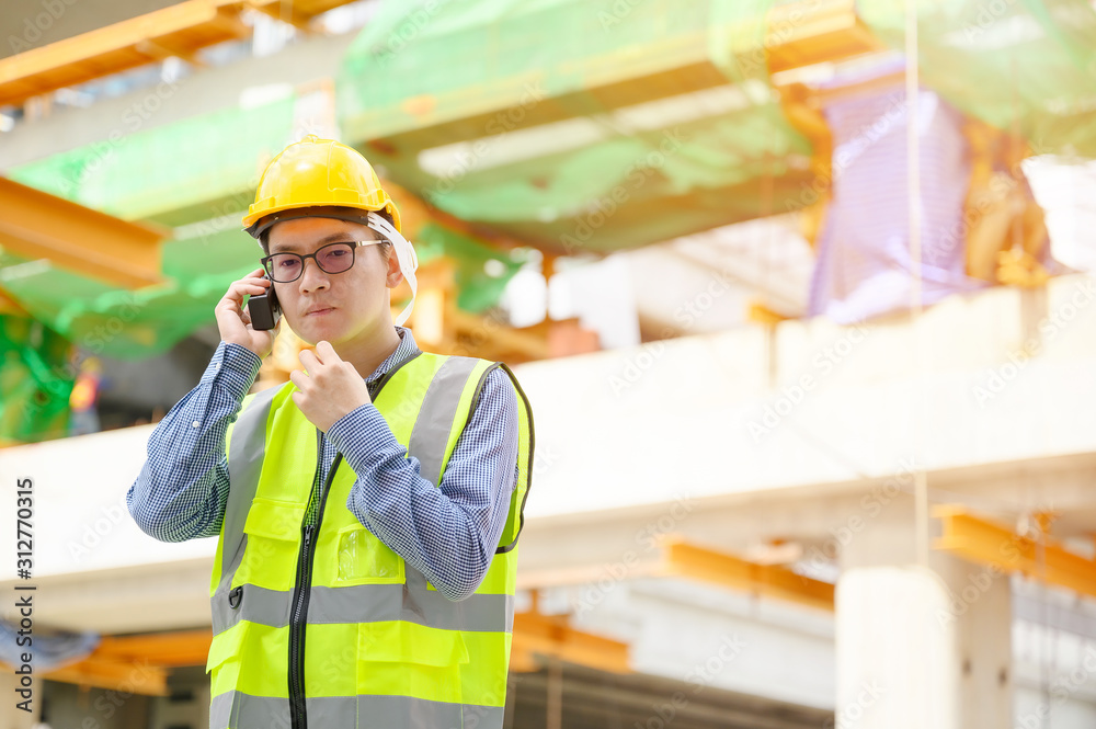 Young asian engineers are working on the construction site. Wear a yellow helmet safety and uniform staff. Hand holding portable radio transceiver for communication