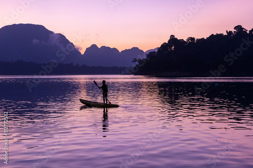 Man stand paddling on his kayak at Ratchaprapa dam, or known as Cheow Lan dam, at sunrise