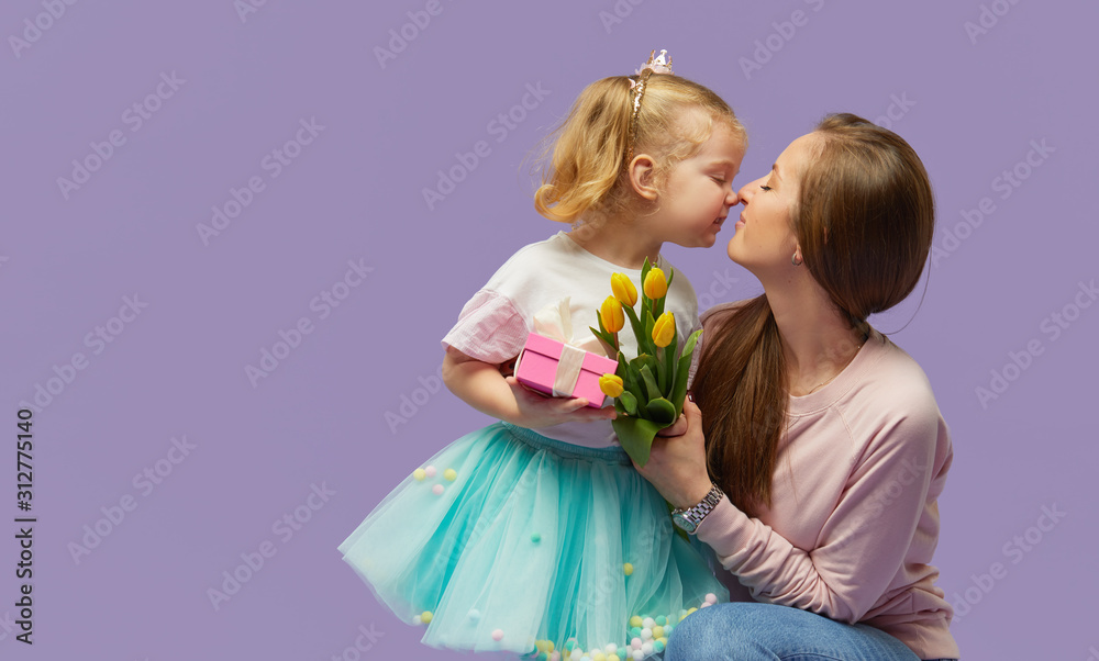8 march card! Little daughter kisses and hugging her mother with yellow flowers tulip and gift box. Purple studio background. Mothers day concept