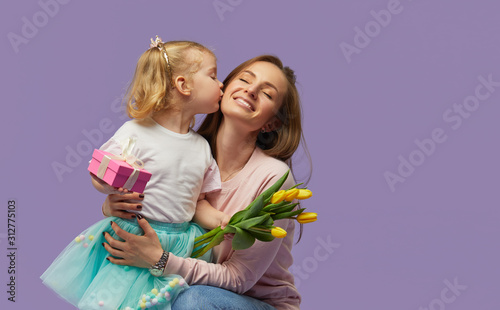Fotografia 8 march card! Little daughter kisses and hugging her mother with yellow flowers tulip and gift box
