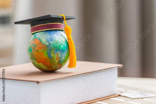 Education to learn study in world. Graduated student studying abroad international idea. Master degree hat on top globe book. Concept of graduate educational for long distane learning anywhere anytime photo