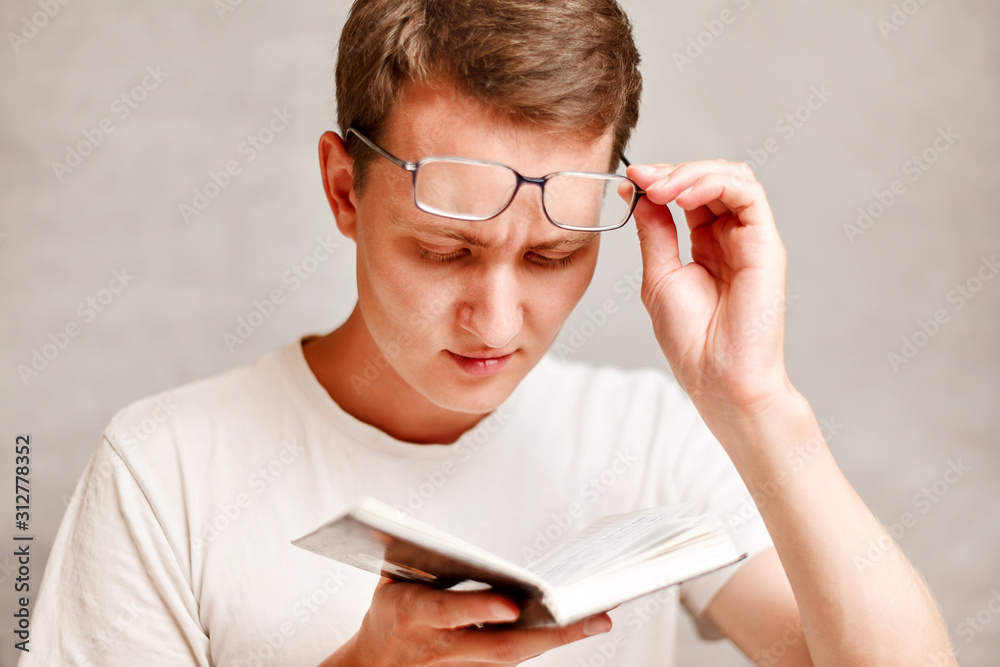 the young man holds glasses with diopter lenses and looking at the book, the problem of myopia, vision correction the young man holds glasses with diopter lenses and looking at the book, the problem of myopia, vision correction