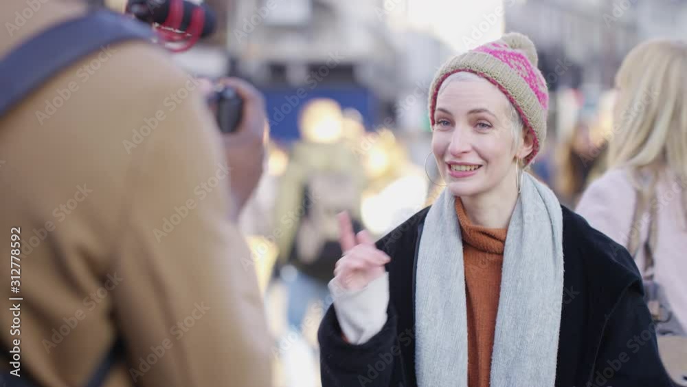 Young trendy female presenter talking to camera on a video blog in the city