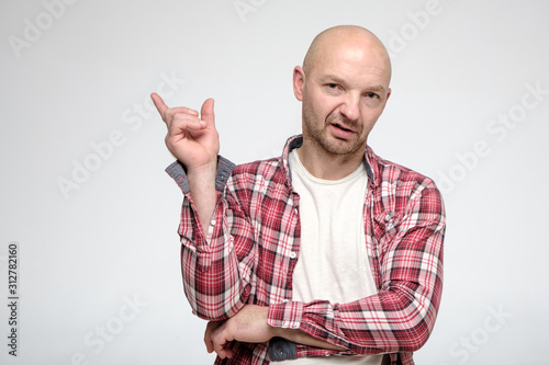 An arrogant bald man points hand to the side and brazenly looks at the camera. Copy space. photo