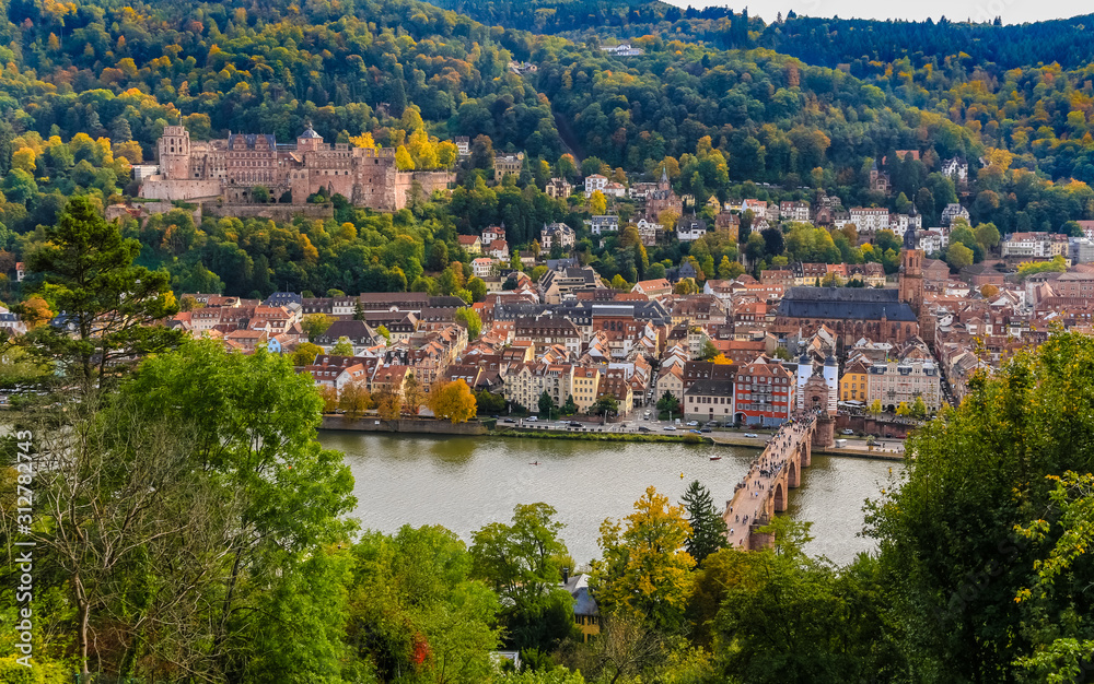 Close aerial panorama of Heidelberg's old town, the castle ruin on Königstuhl hill, the church Heiliggeistkirche and the Karl Theodor Bridge on Neckar river seen from the Philosopher’s Path in autumn.