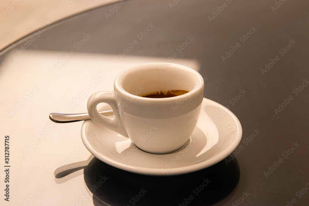 Simple white espresso cup and saucer with sppon on a round table.